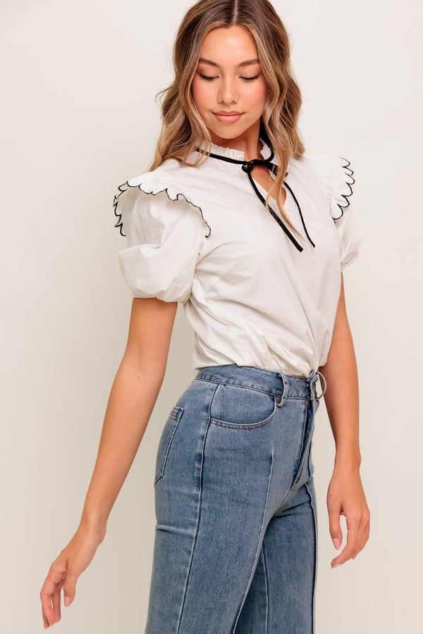 A solid woven top featuring ruffed neckline with tie, scallop edge shoulder and short sleeve
