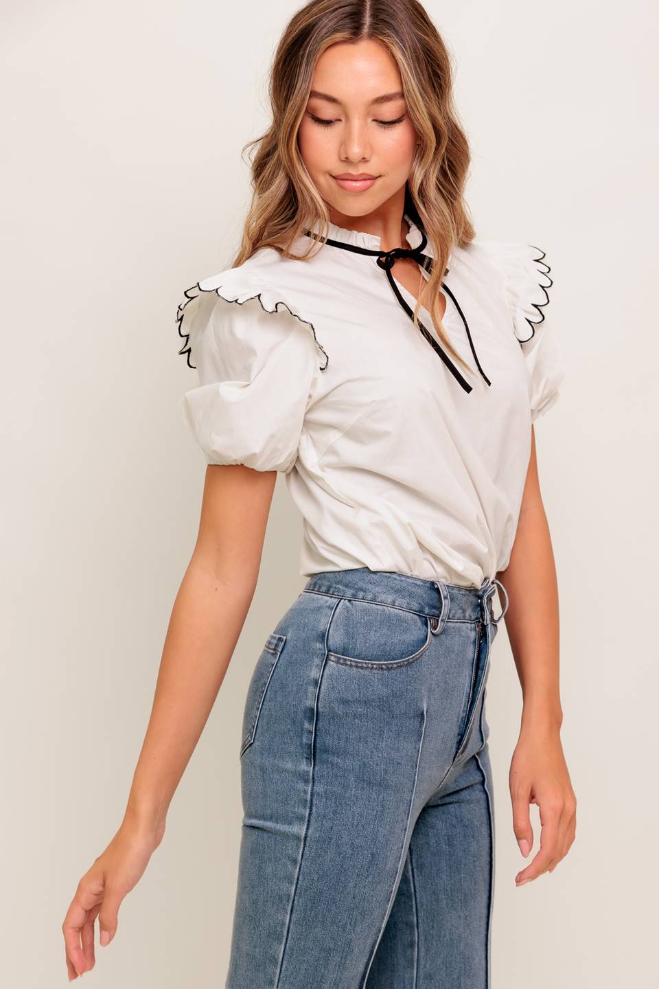 A solid woven top featuring ruffed neckline with tie, scallop edge shoulder and short sleeve