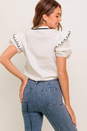 A solid woven top featuring ruffed neckline with tie, scallop edge shoulder and short sleeve