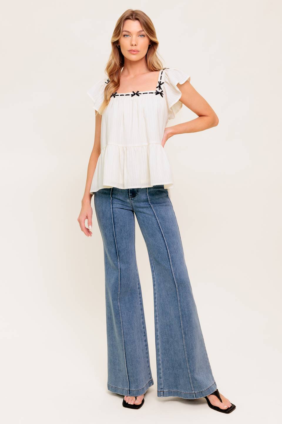 A solid woven top featuring square neckline, short flutter sleeve, ribbon trim and ruffled hemline.