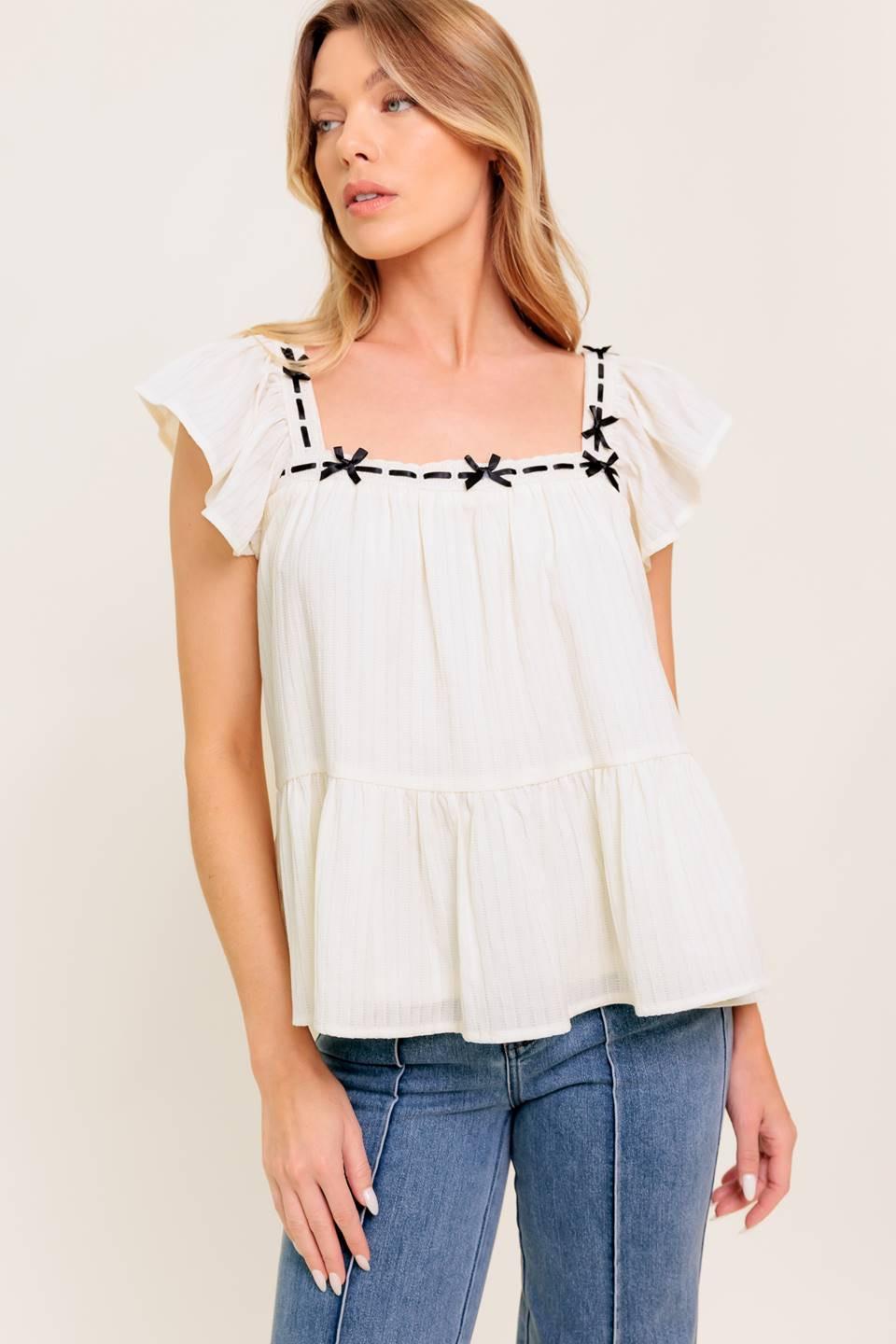 A solid woven top featuring square neckline, short flutter sleeve, ribbon trim and ruffled hemline.