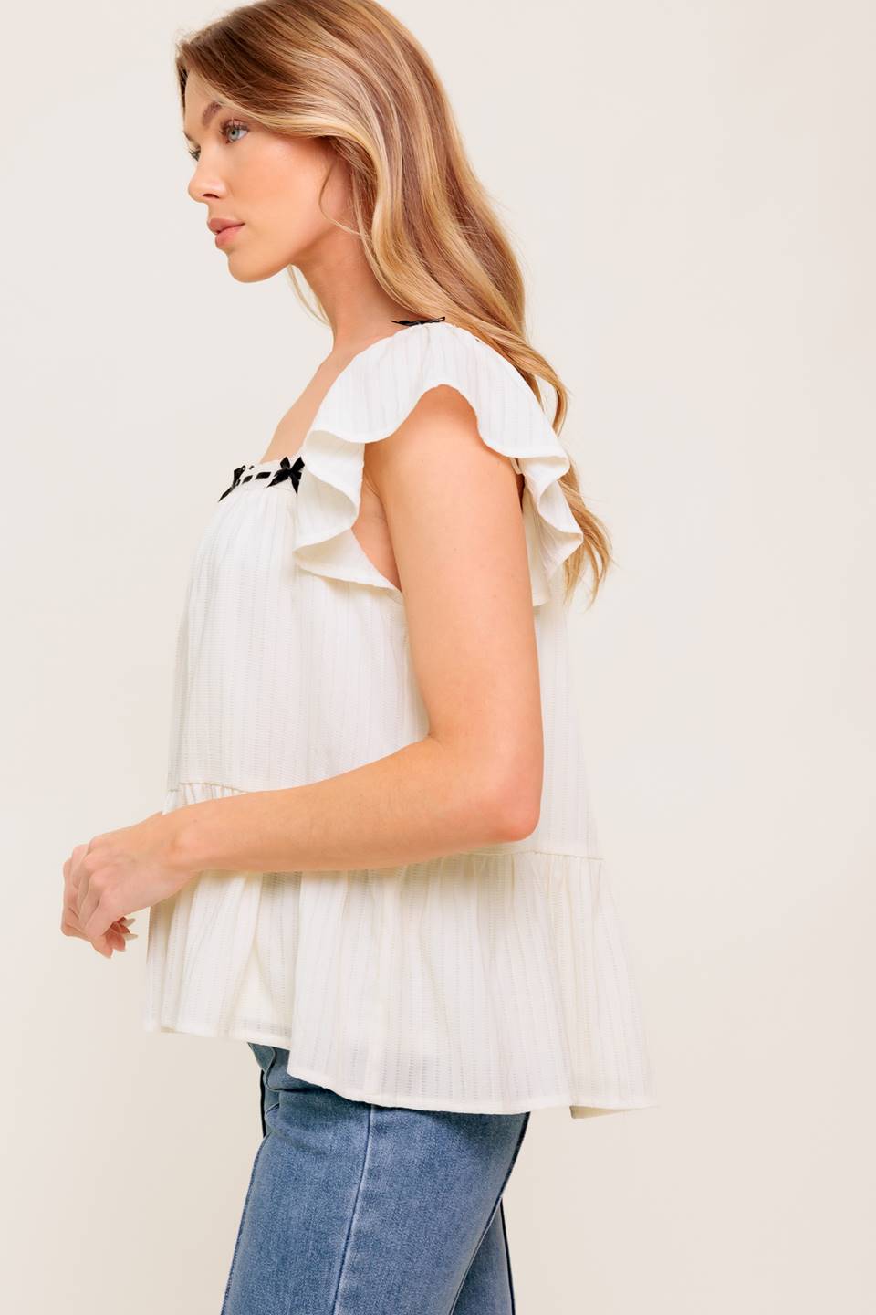 A solid woven top featuring square neckline, short flutter sleeve, ribbon trim and ruffled hemline.
