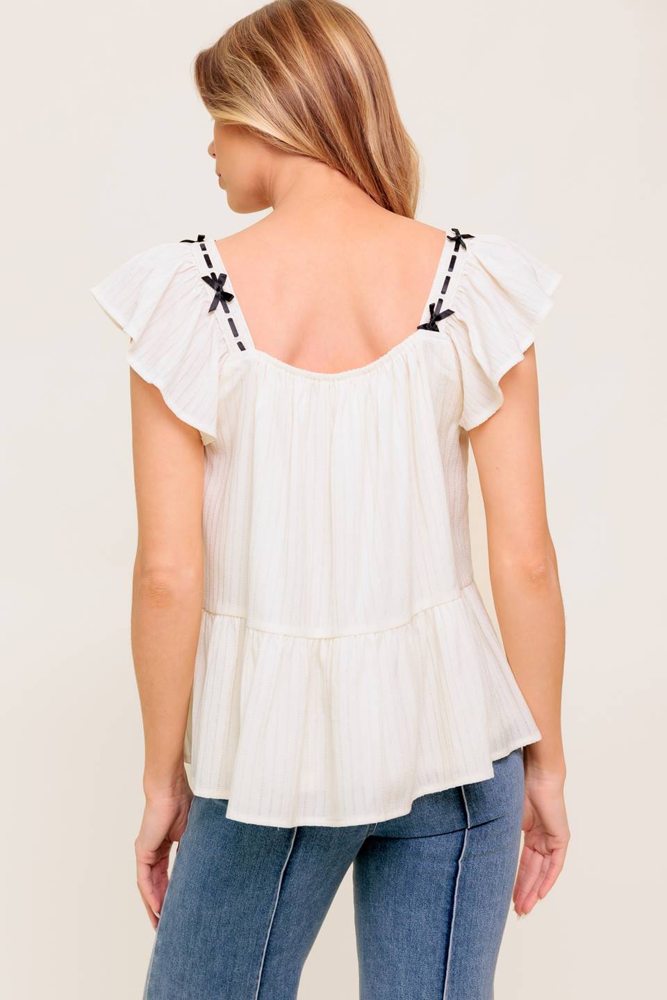 A solid woven top featuring square neckline, short flutter sleeve, ribbon trim and ruffled hemline.