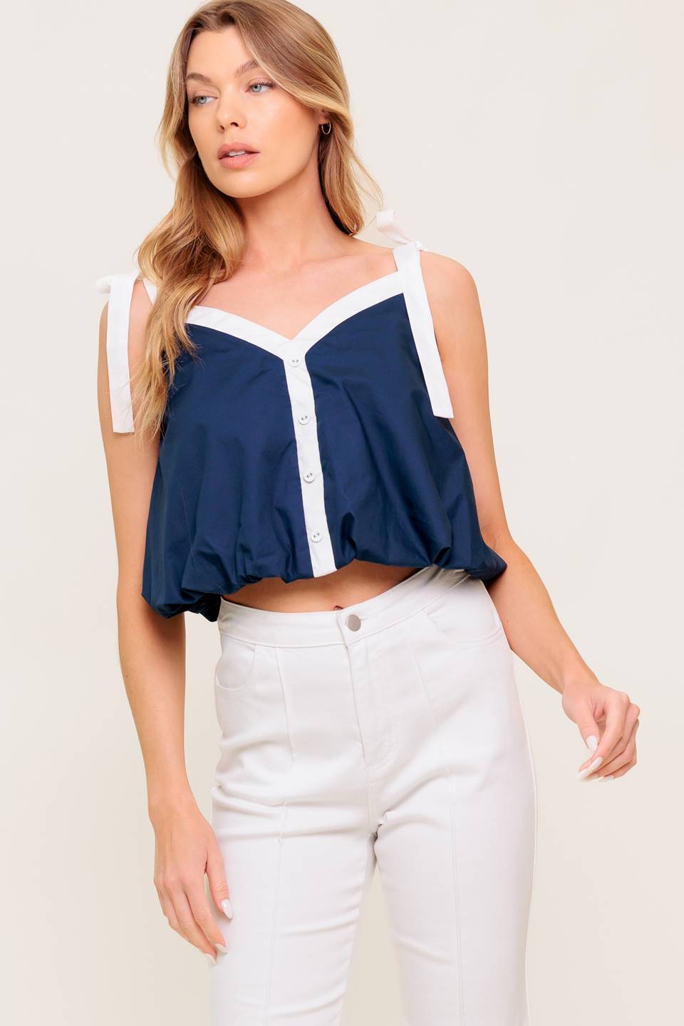 A solid woven top featuring shoulder tie, button detail and bubble hemline.