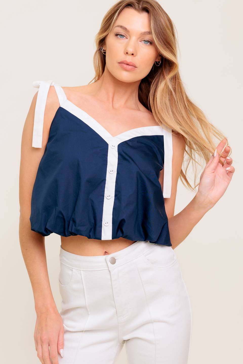 A solid woven top featuring shoulder tie, button detail and bubble hemline.