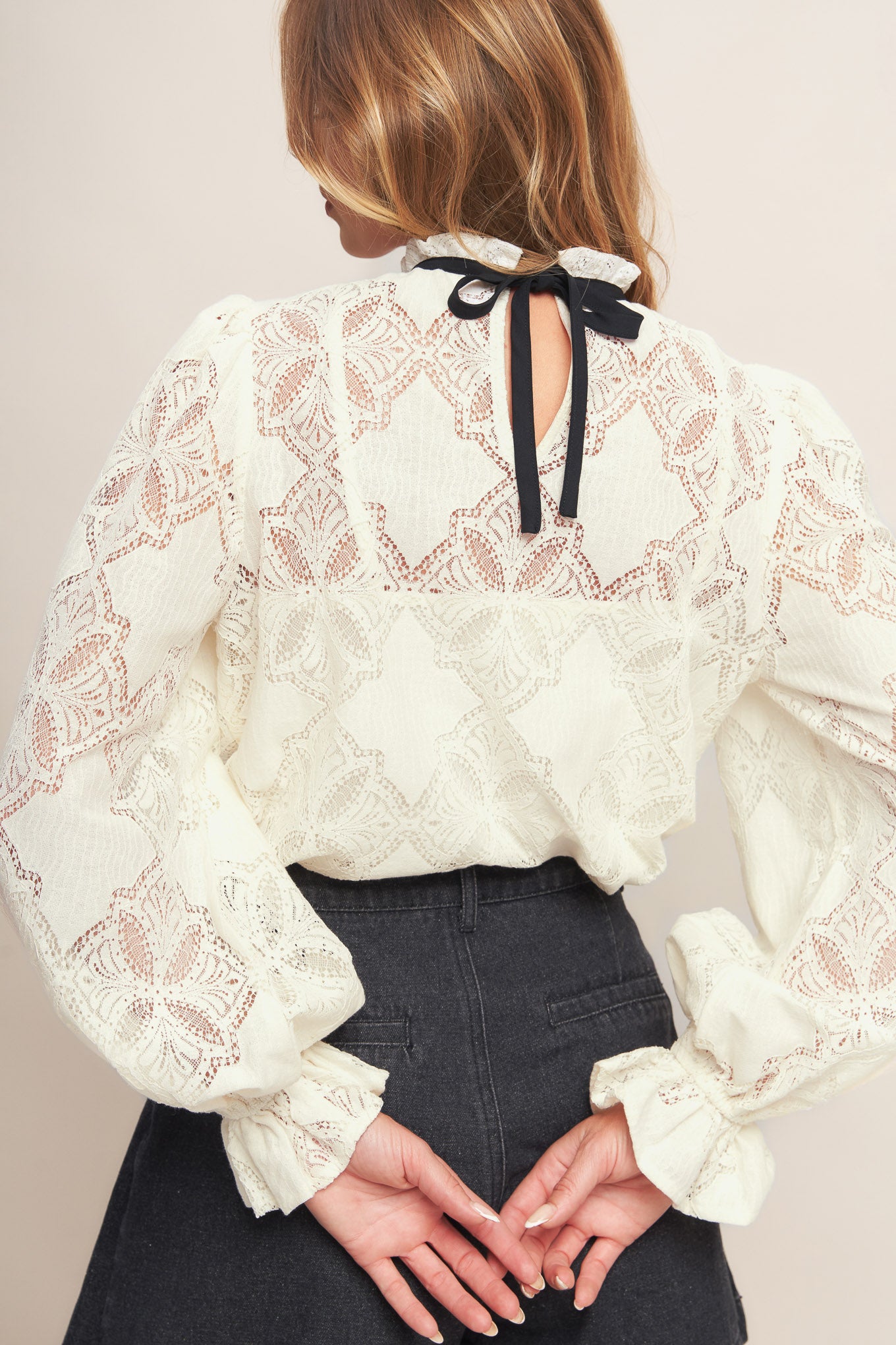 A woven lace top featuring ruffled high neckline with contrasting band, long sleeve with ruffled cuff, cami and back neck tie closure

