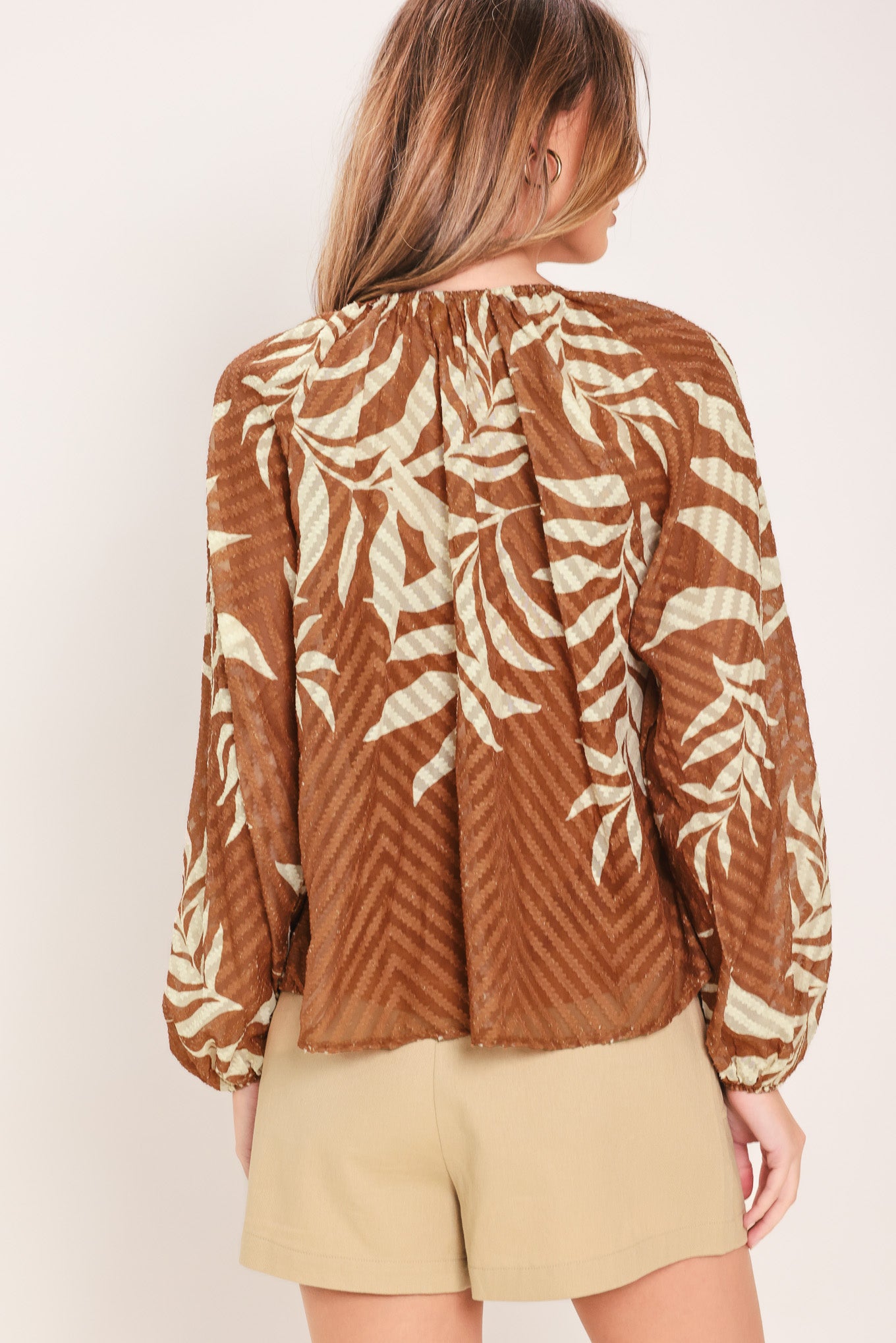 Woman wearing a long sleeve brown and beige leaf patterned blouse | Flying Tomato
