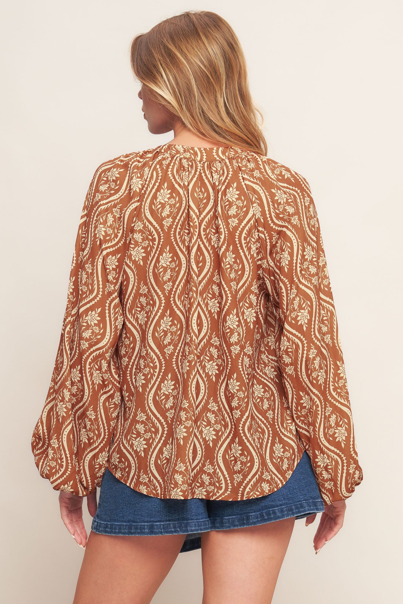 A printed woven top featuring round neckline with V front and long raglan sleeve