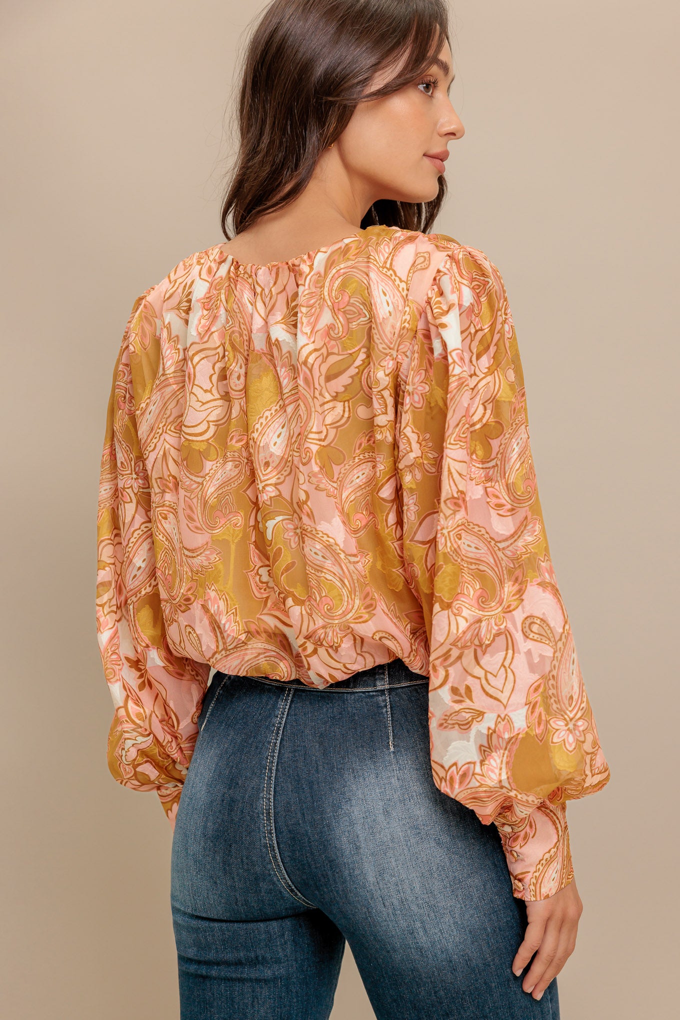 A printed woven jacquard top featuring round neckline, long blouson sleeve with cuff and back neck button closure