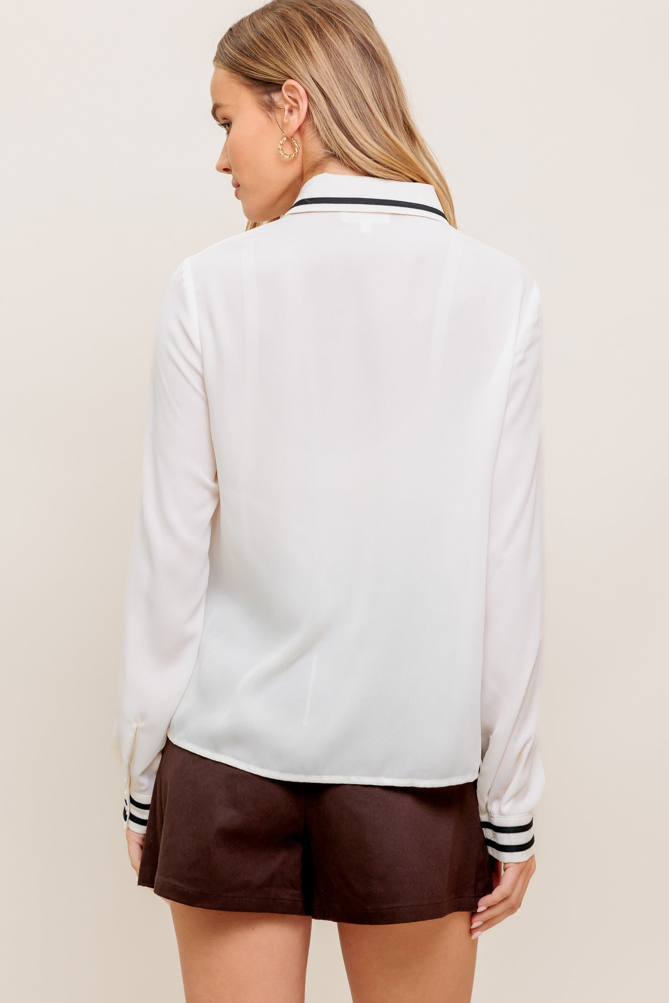 A solid woven top featuring collar, hidden button down and long sleeve