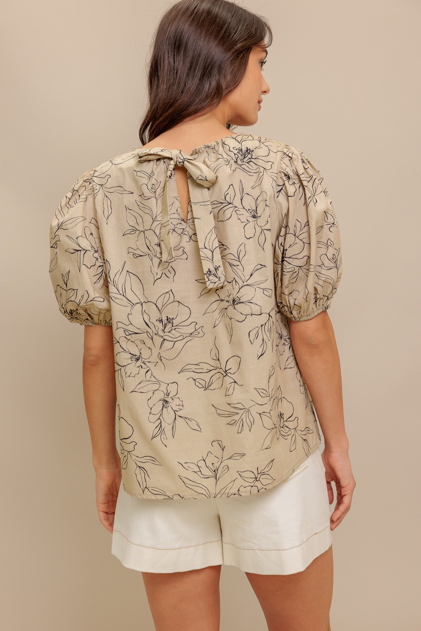 A printed woven top featuring round neckline, short puff sleeve and back neck tie closure