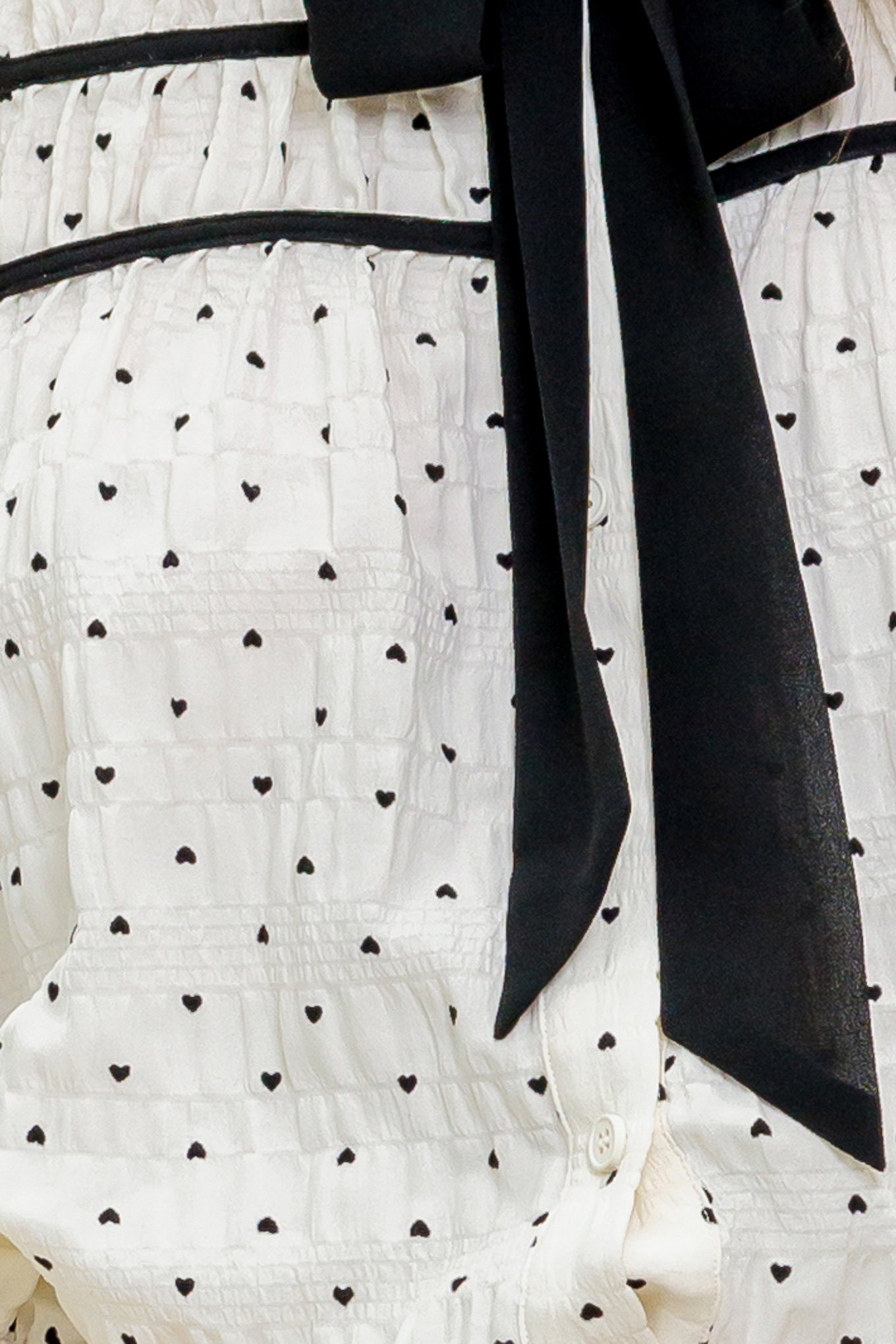 A heart printed woven top featuring collar, contrasting bow tie, long sleeve with smocked cuff and front button closure