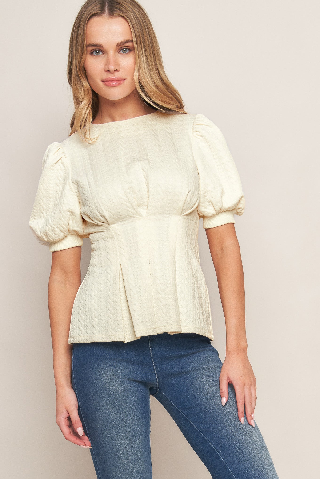 A textured woven top featuring round neckline, short puff sleeve, tapered waist and peplum