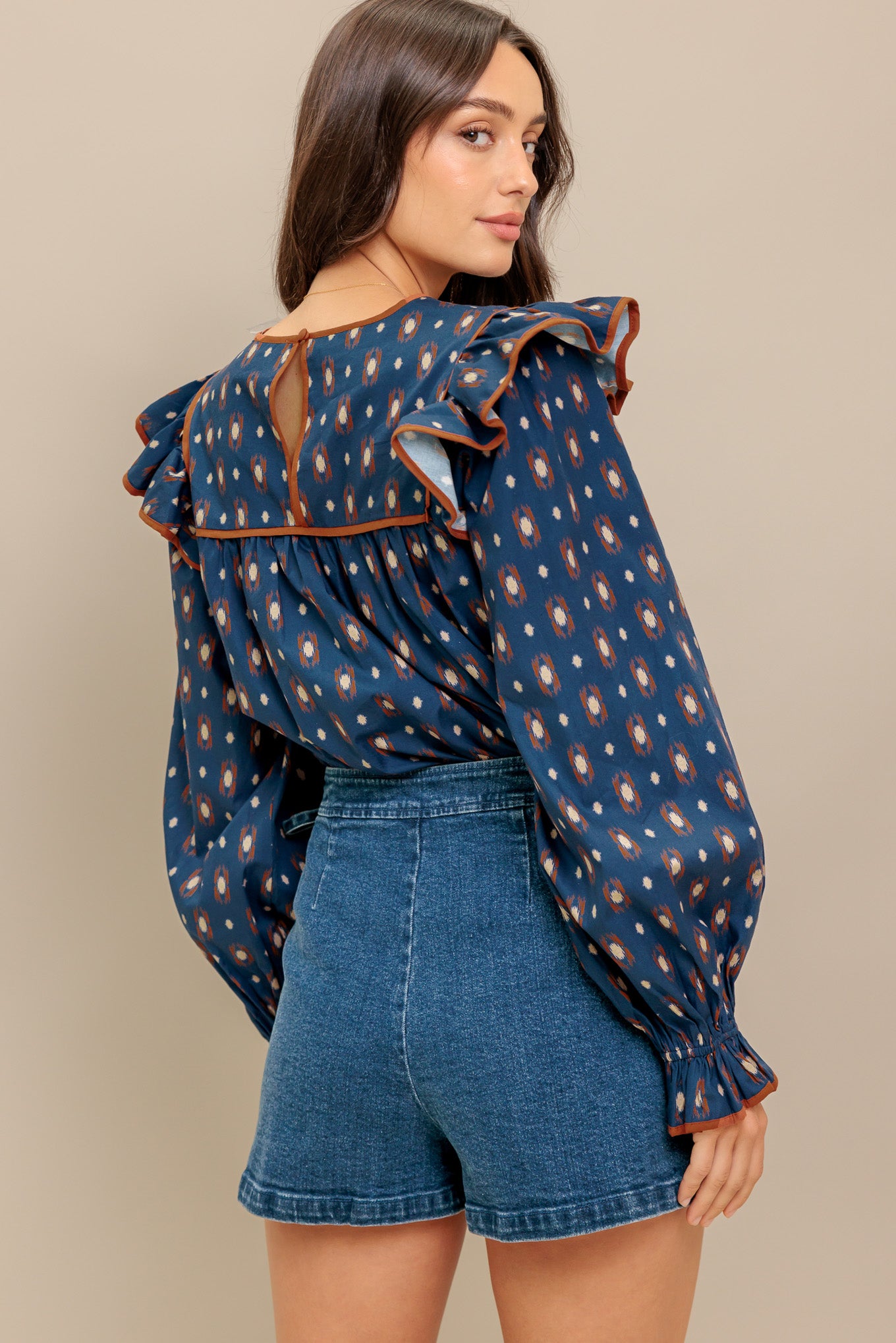 A printed woven top featuring round neckline, yoke, ruffled shoulder, long sleeve and back neck button closure
