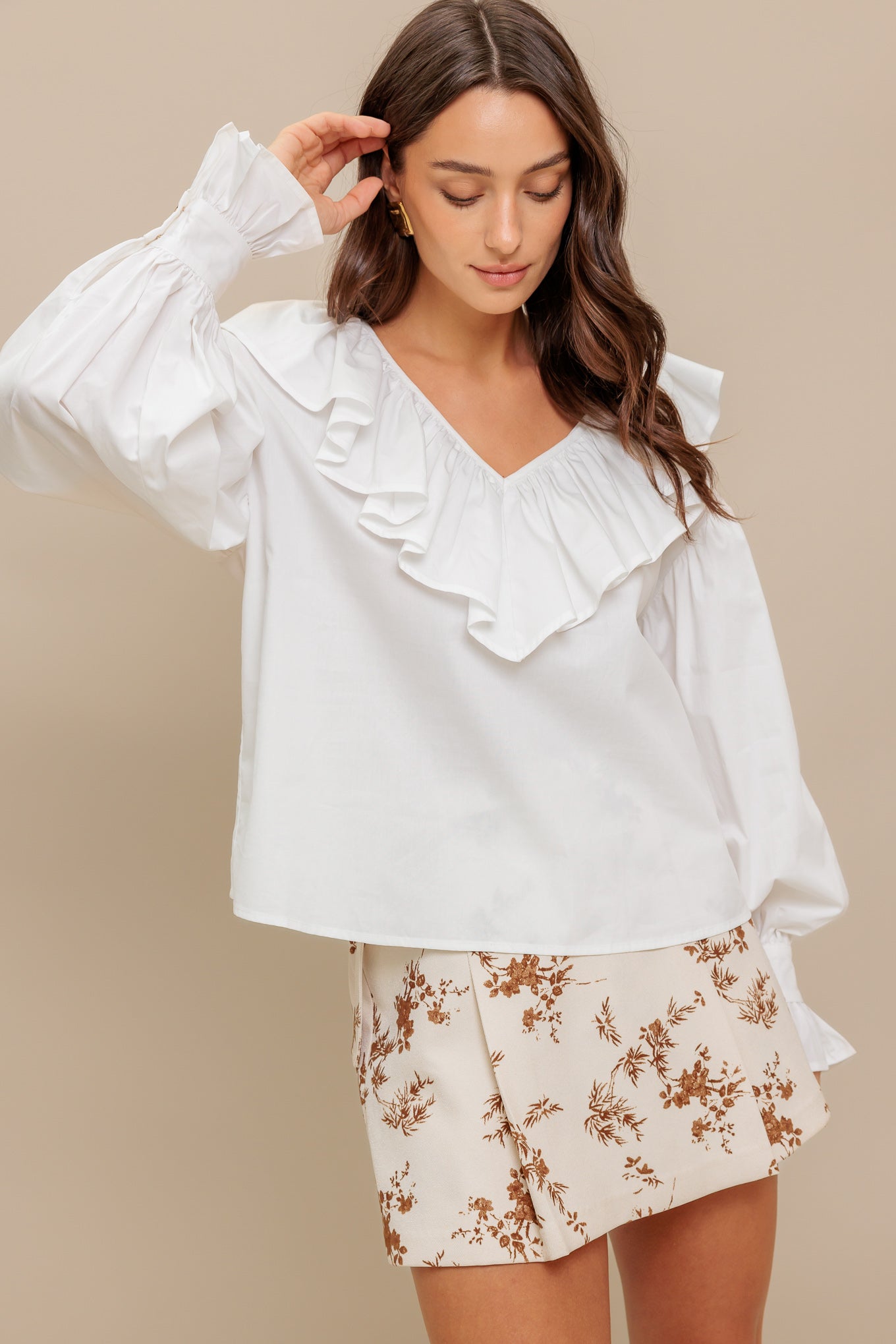 A solid woven top featuring V neckline with ruffles and long puff sleeve with cuff