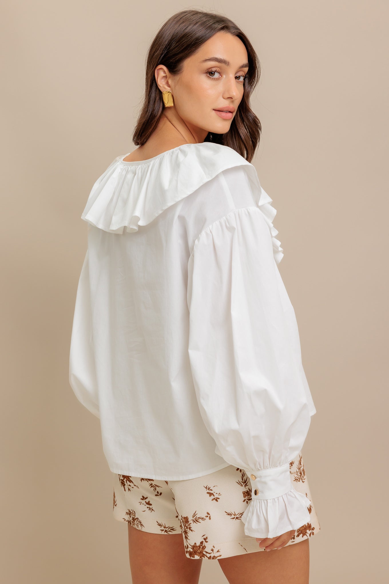 A solid woven top featuring V neckline with ruffles and long puff sleeve with cuff