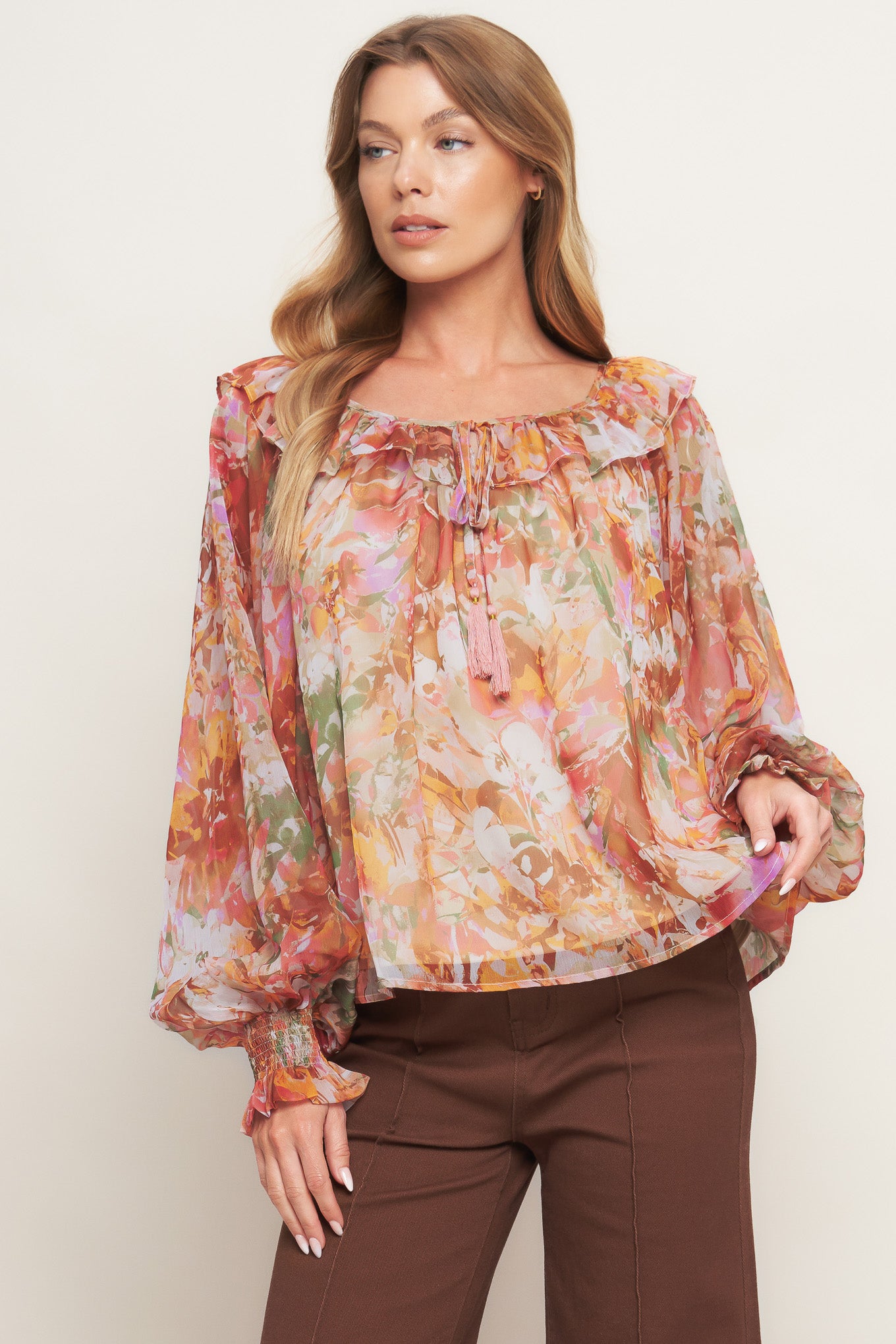A printed woven top featuring wide round neckline with ruffles, front tie and tassel, long blouson sleeve with ruffled cuff and lining