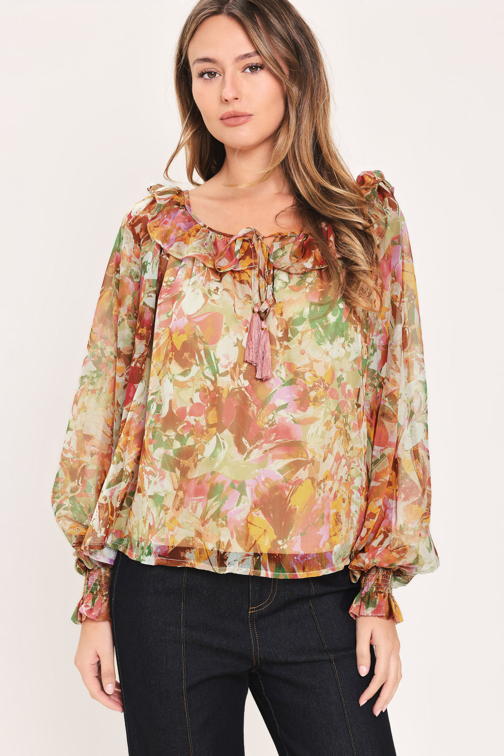 Woman wearing a long sleeve, u-neckline floral rust multicolor blouse with small bow detail and tassels on the center chest | Flying Tomato