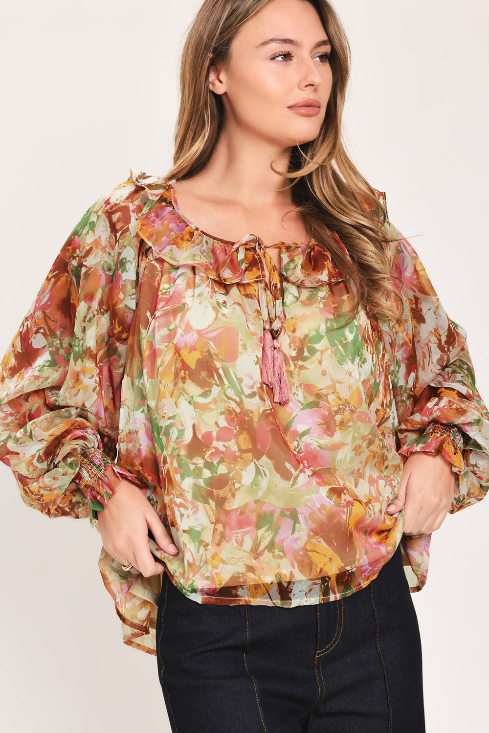 Woman wearing a long sleeve, u-neckline floral rust multicolor blouse with small bow detail and tassels on the center chest | Flying Tomato