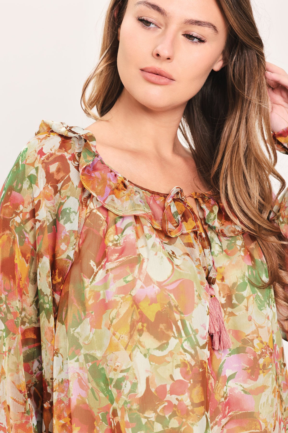 Woman wearing a long sleeve, u-neckline floral rust multicolor blouse with small bow detail and tassels on the center chest | Flying Tomato