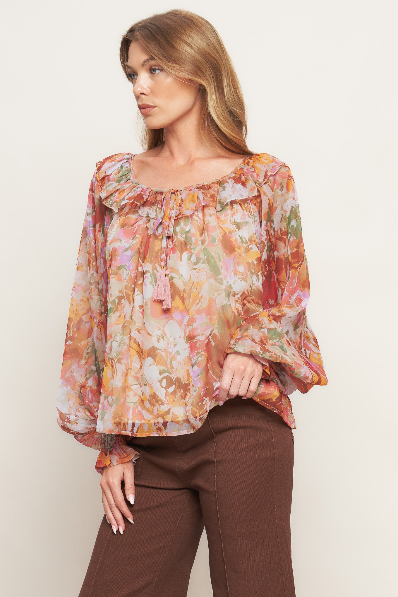 A printed woven top featuring wide round neckline with ruffles, front tie and tassel, long blouson sleeve with ruffled cuff and lining