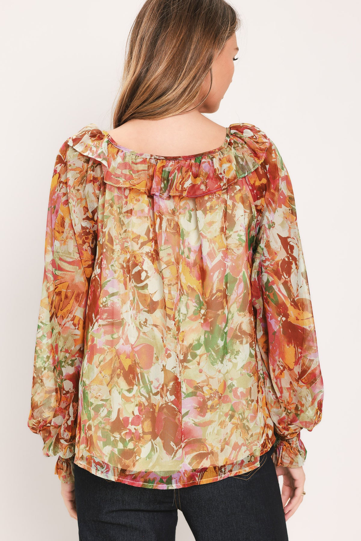 Woman wearing a long sleeve, u-neckline floral rust multicolor blouse with small bow detail and tassels on the center chest | Flying Tomato