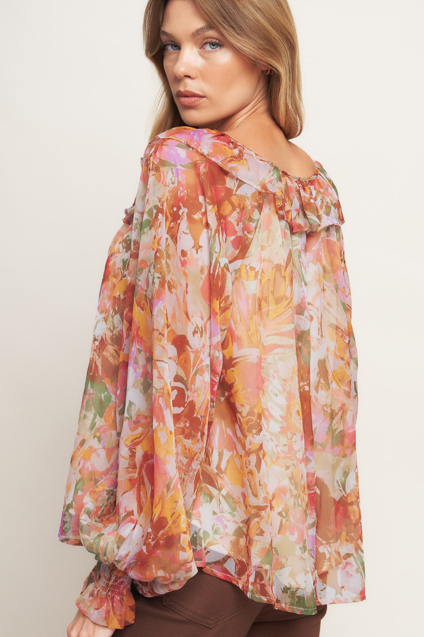 A printed woven top featuring wide round neckline with ruffles, front tie and tassel, long blouson sleeve with ruffled cuff and lining