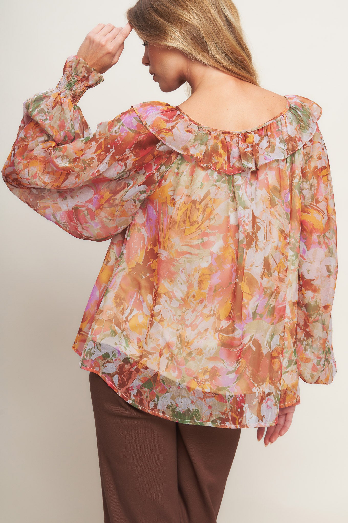 A printed woven top featuring wide round neckline with ruffles, front tie and tassel, long blouson sleeve with ruffled cuff and lining