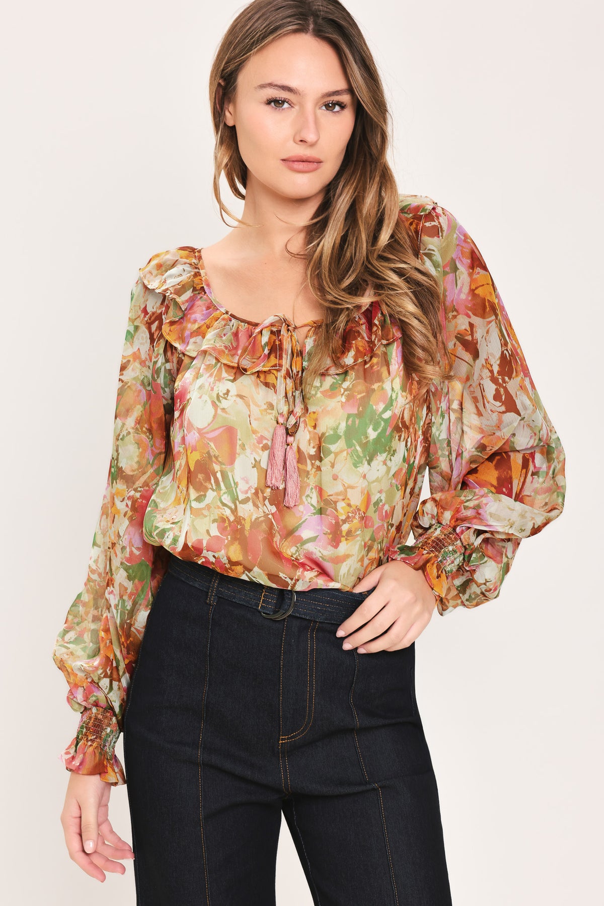 Woman wearing a long sleeve, u-neckline floral rust multicolor blouse with small bow detail and tassels on the center chest | Flying Tomato