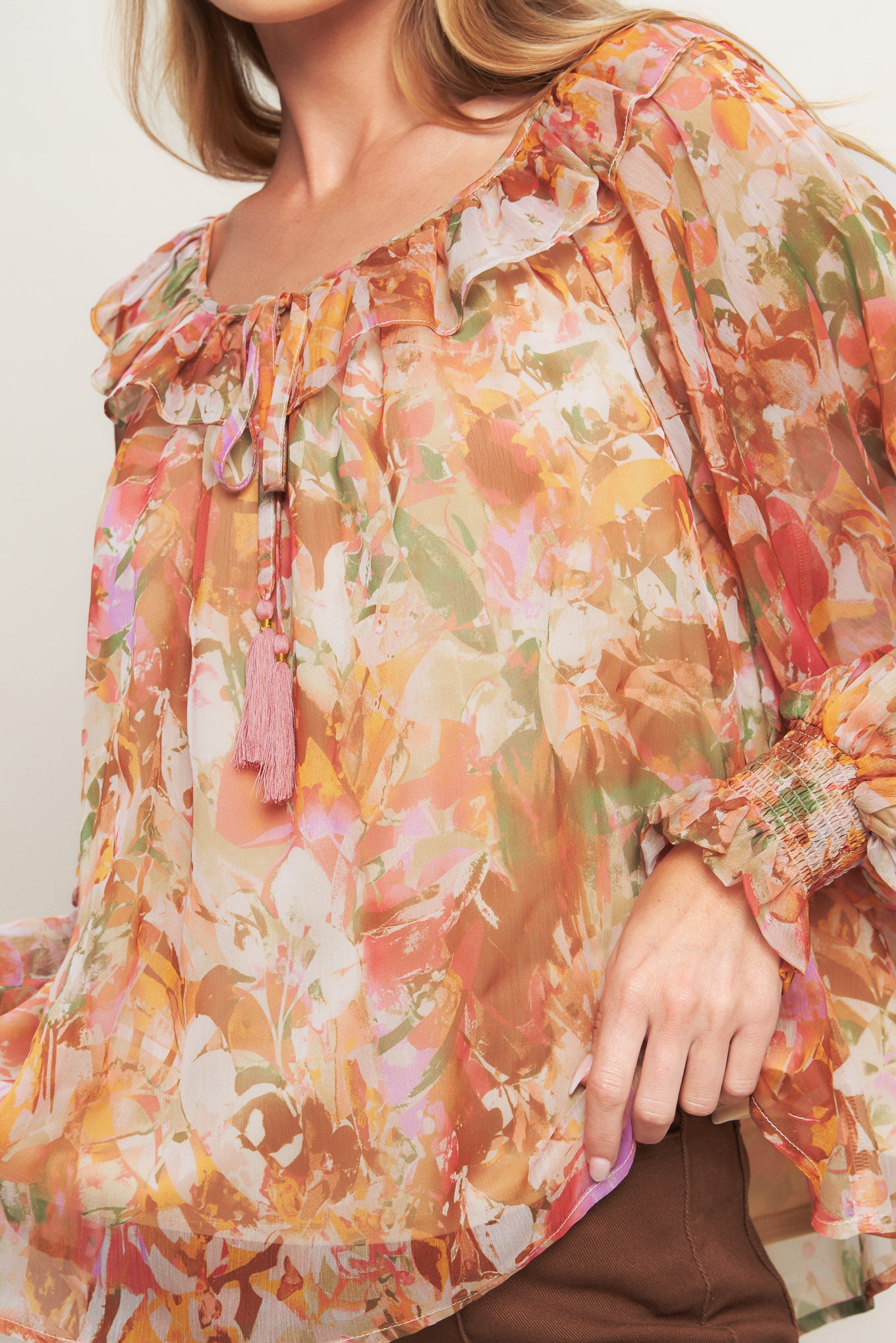 A printed woven top featuring wide round neckline with ruffles, front tie and tassel, long blouson sleeve with ruffled cuff and lining