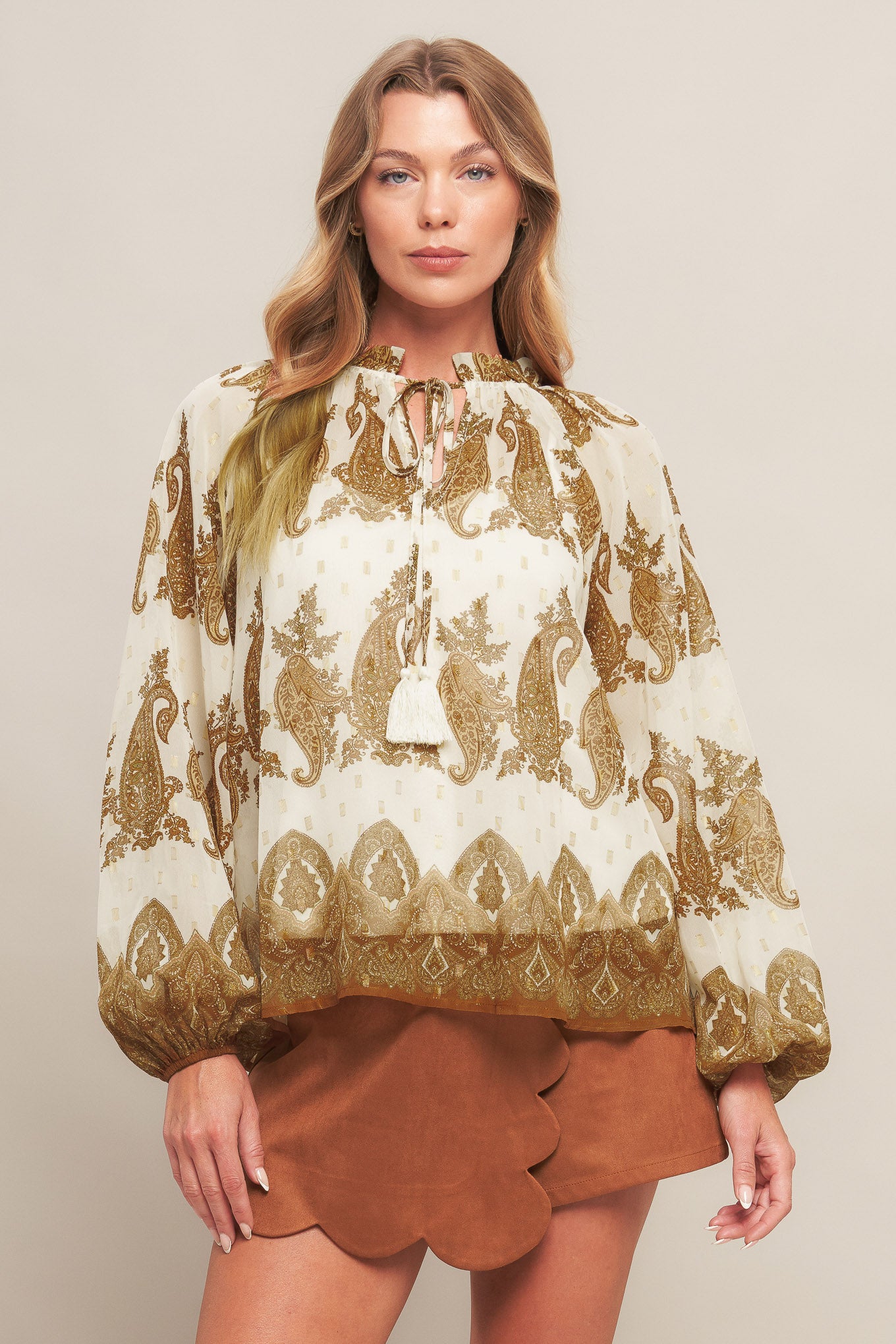 A printed woven top featuring ruffled round neckline with front tie tassel and long sleeve