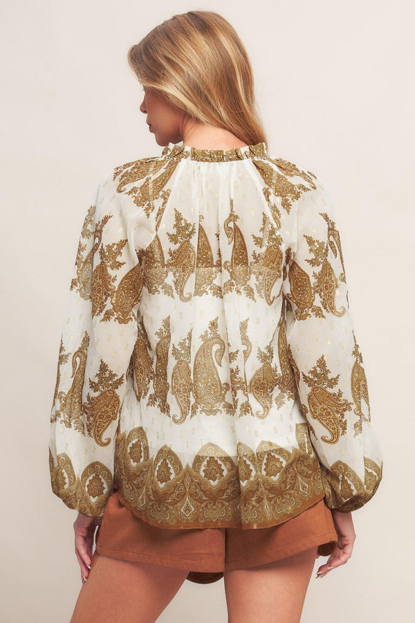 A printed woven top featuring ruffled round neckline with front tie tassel and long sleeve