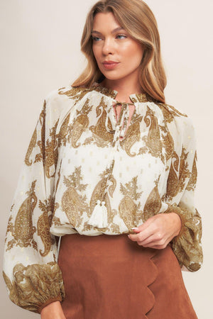 A printed woven top featuring ruffled round neckline with front tie tassel and long sleeve