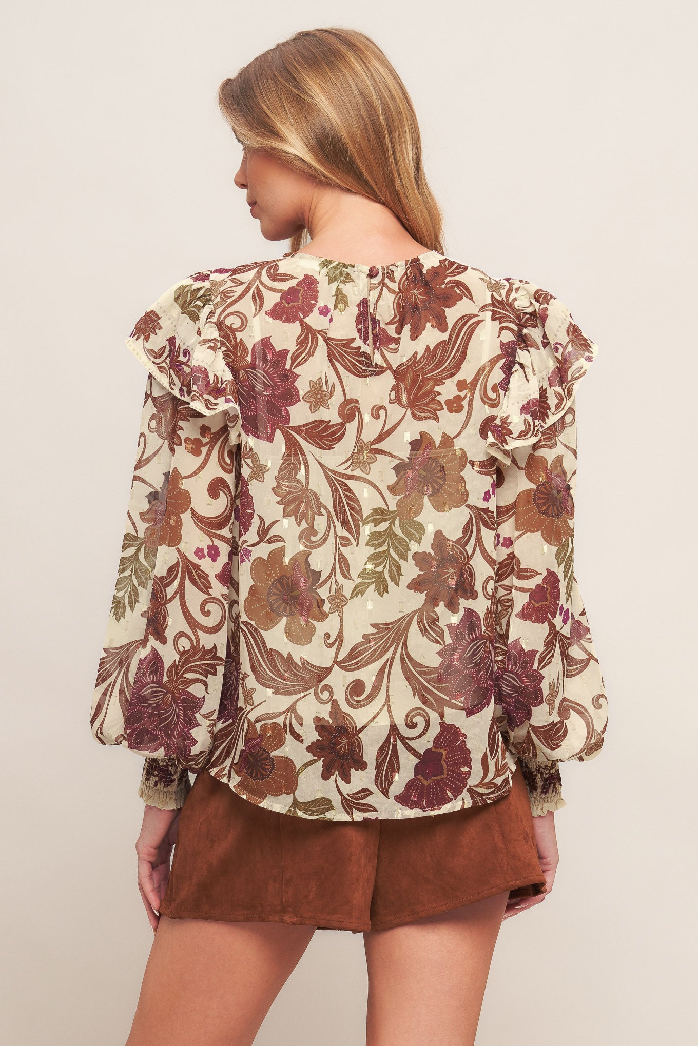 A printed woven top featuring round neckline, long sleeve with cuff and ruffled shoulder and back neck button closure