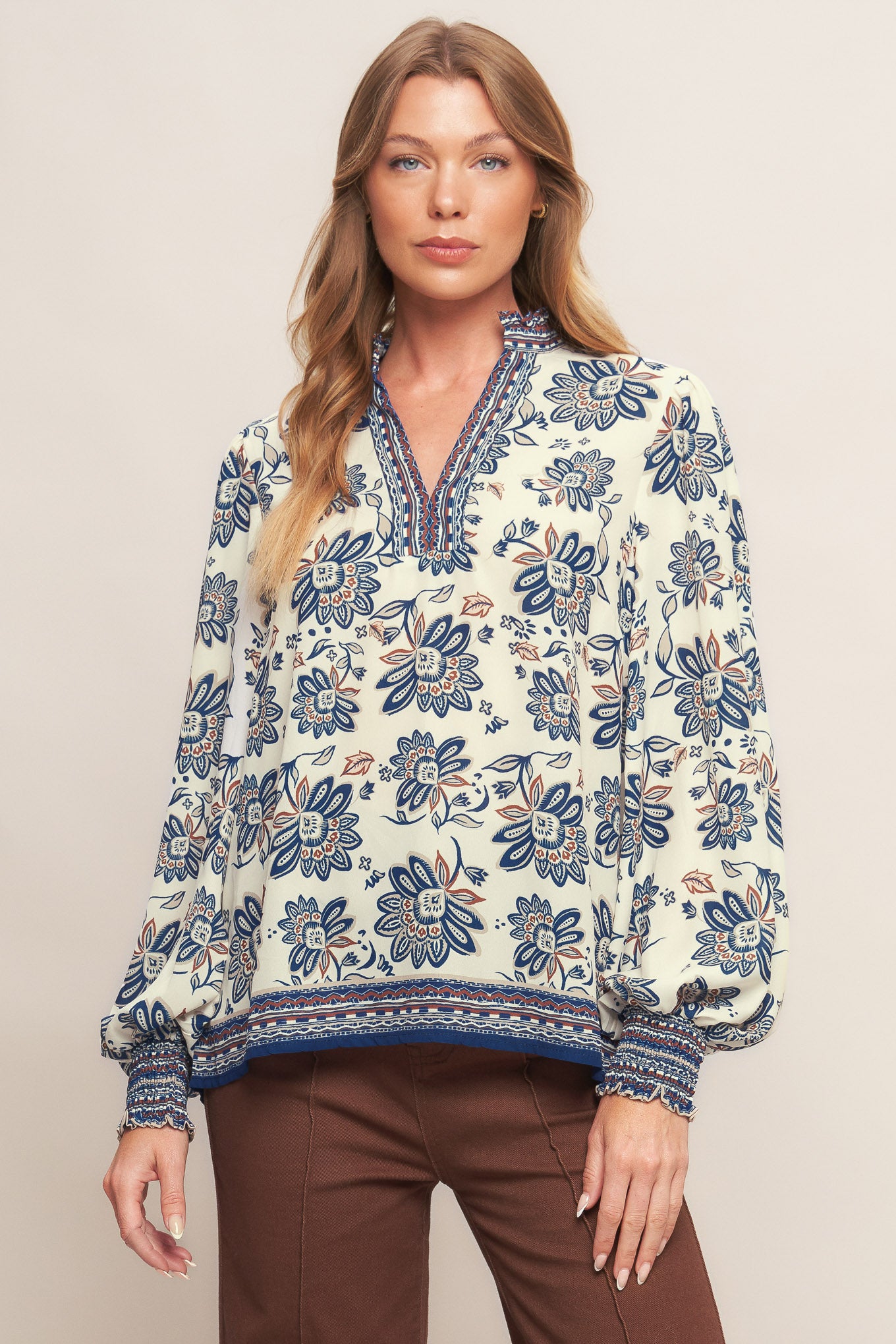 A printed woven top featuring ruffled neckline with V front and long sleeve with smocked cuff
