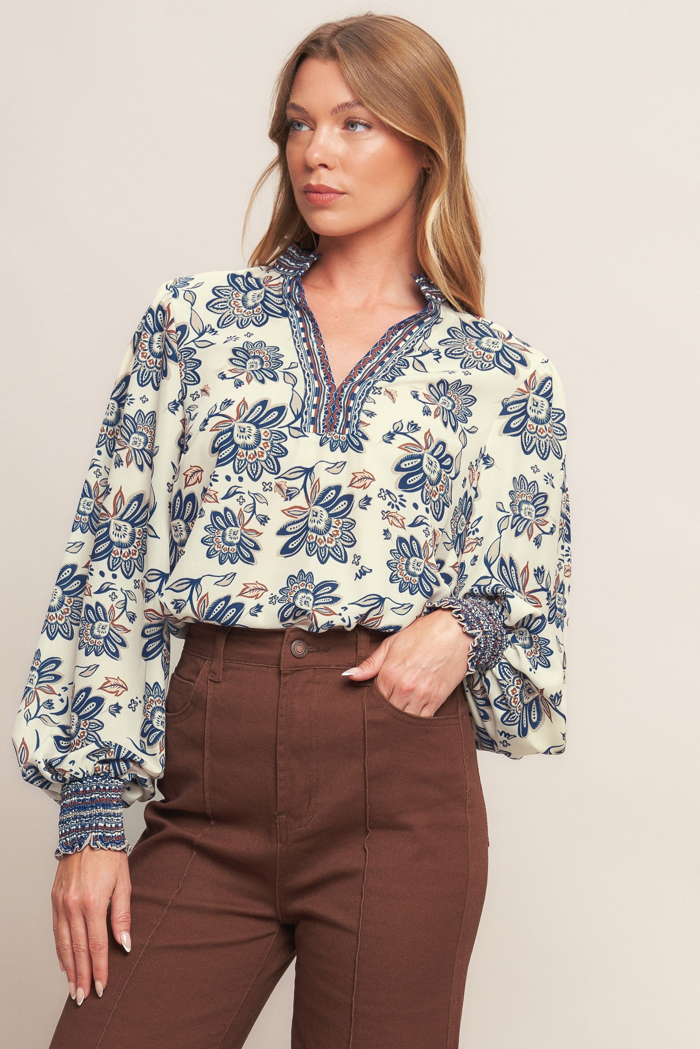 A printed woven top featuring ruffled neckline with V front and long sleeve with smocked cuff