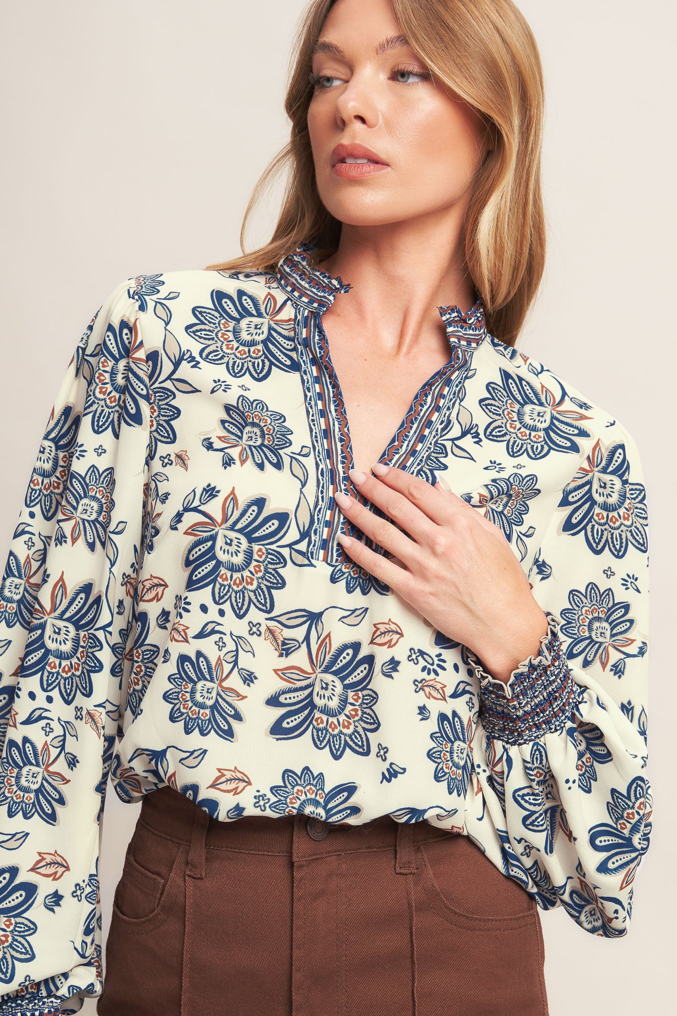 A printed woven top featuring ruffled neckline with V front and long sleeve with smocked cuff