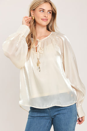 Woman wearing an ivory champagne long sleeve blouse with a front tie and charms | Flying Tomato