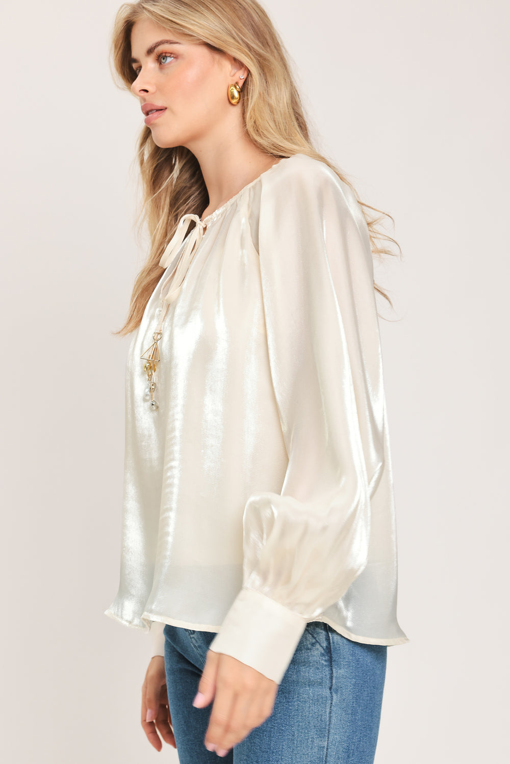 Woman wearing an ivory champagne long sleeve blouse with a front tie and charms | Flying Tomato
