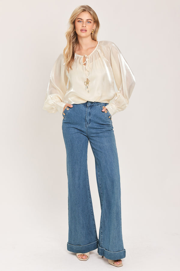 Woman wearing an ivory champagne long sleeve blouse with a front tie and charms | Flying Tomato