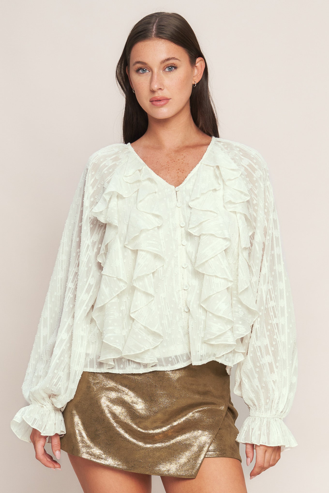 A textured woven top featuring V neckline, front button down, ruffled bodice and long blouson sleeve with ruffled cuff