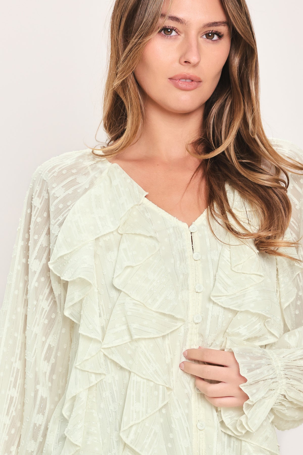 Woman wearing a cream long sleeve blouse with ruffles running down the torso | Flying Tomato