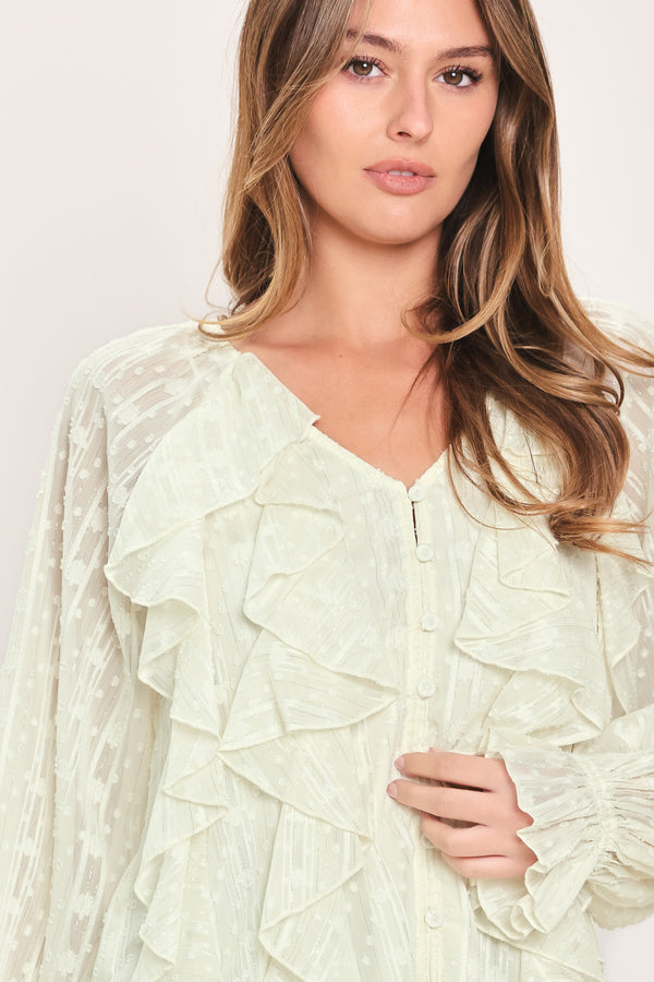Woman wearing a cream long sleeve blouse with ruffles running down the torso | Flying Tomato