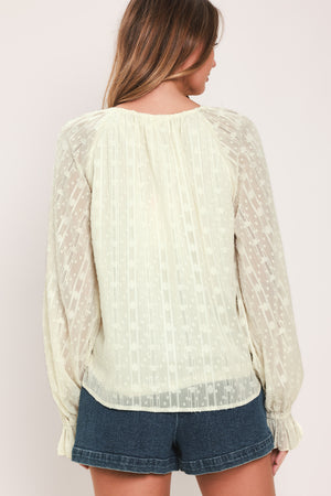 Woman wearing a cream long sleeve blouse with ruffles running down the torso | Flying Tomato