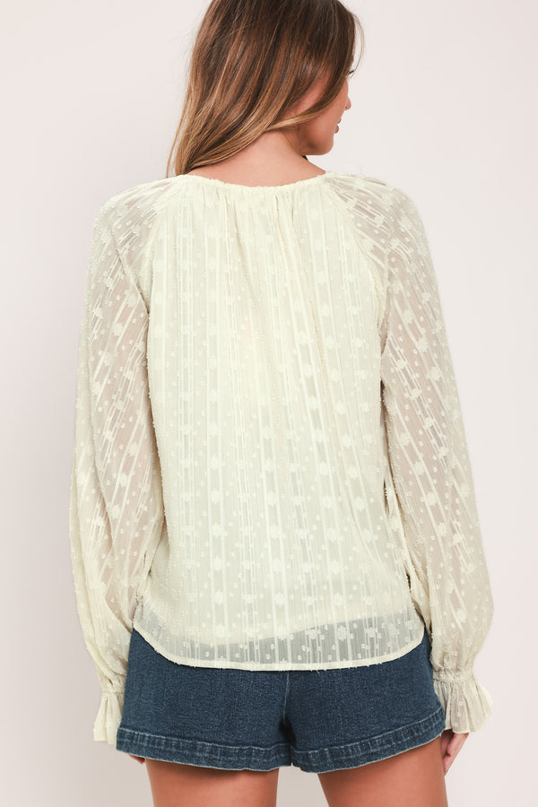 Woman wearing a cream long sleeve blouse with ruffles running down the torso | Flying Tomato