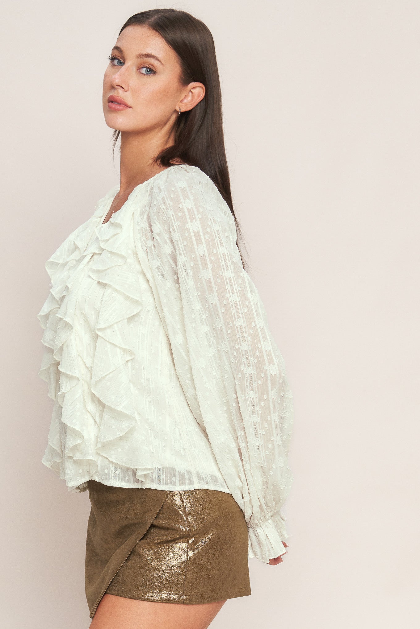 A textured woven top featuring V neckline, front button down, ruffled bodice and long blouson sleeve with ruffled cuff