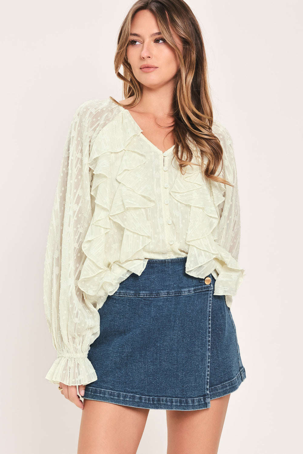 Woman wearing a cream long sleeve blouse with ruffles running down the torso | Flying Tomato