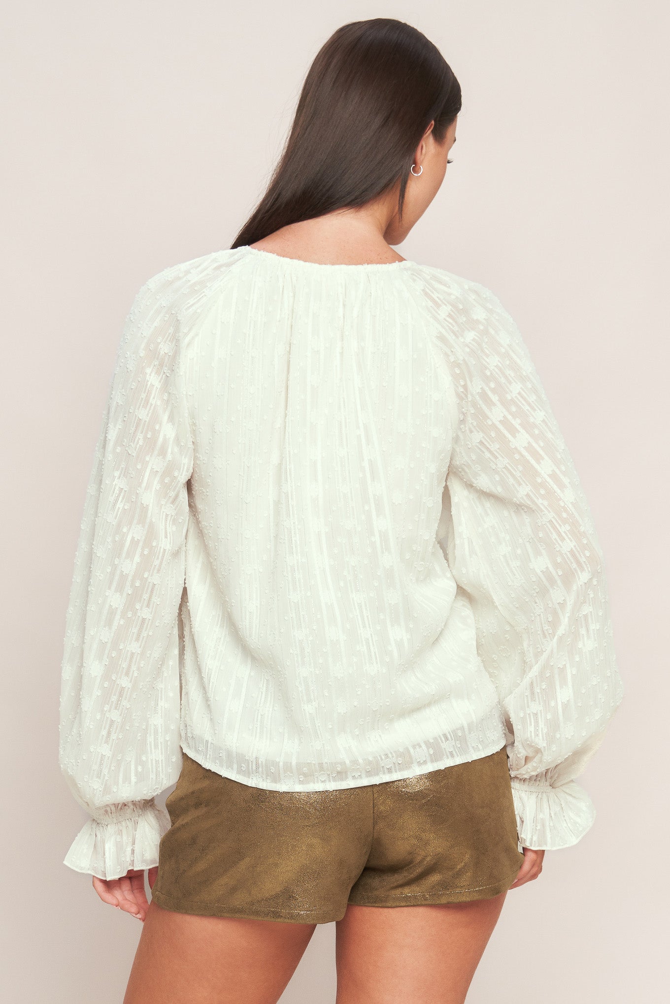 A textured woven top featuring V neckline, front button down, ruffled bodice and long blouson sleeve with ruffled cuff