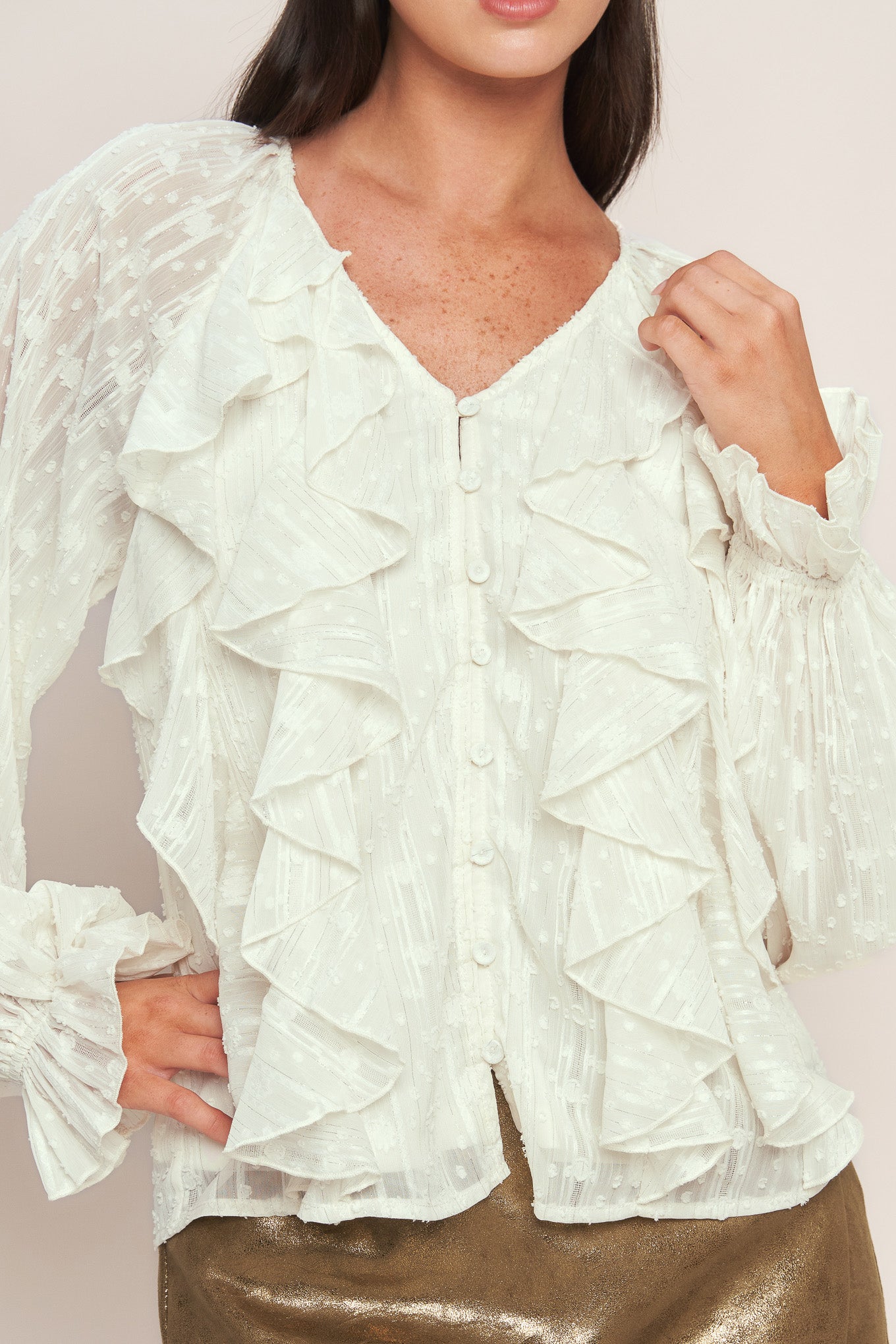 A textured woven top featuring V neckline, front button down, ruffled bodice and long blouson sleeve with ruffled cuff