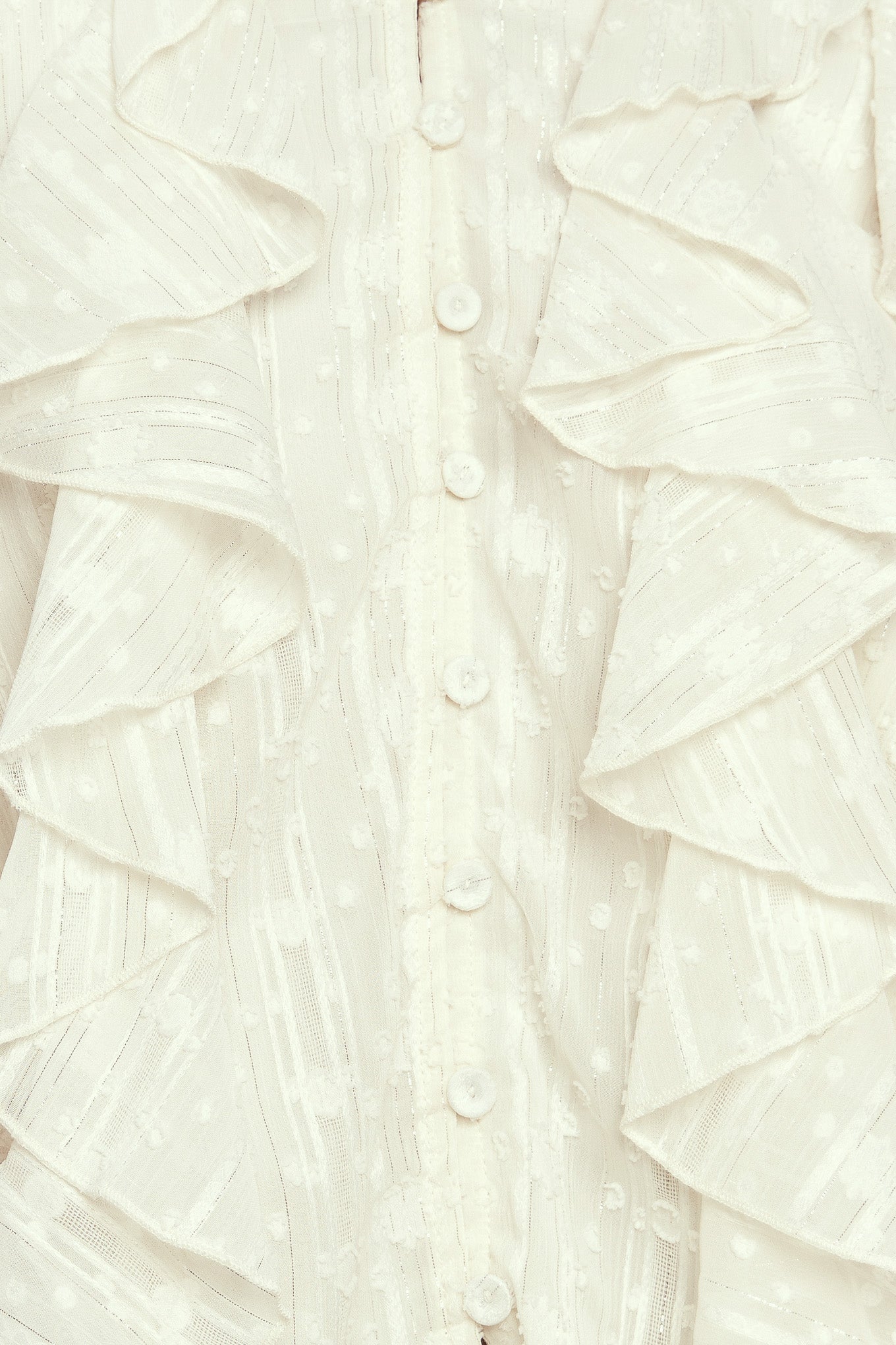 A textured woven top featuring V neckline, front button down, ruffled bodice and long blouson sleeve with ruffled cuff